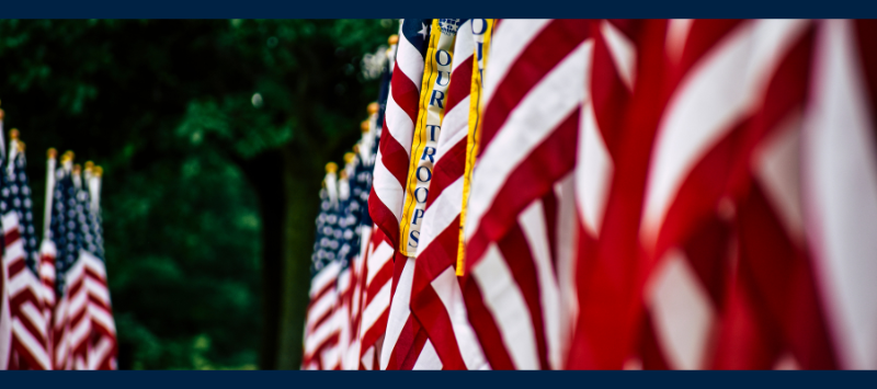 Field of US flags with streamer reading Our Troops
