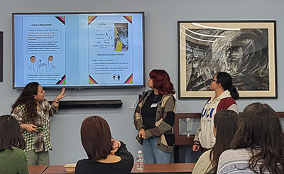 UCI students Chloe Ford (left), Inez Rosales (right), and Kaye Regalado (far right), present the zine they created.